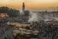 Djemaa el Fna in Marrakesch bei Sonnenuntergang mit zahlreichen Essensständen und der Koutoubia-Moschee im Hintergrund.