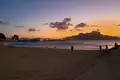 Sonnenuntergang über einem Strand mit Menschen, die am Ufer entlang gehen.