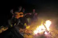 Reisende sitzen um ein Lagerfeuer und spielen Gitarre.