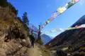 Wanderer auf einem Bergpfad mit bunten Gebetsfahnen und Blick auf die Berge.