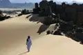 Person durchquert eine Sanddüne in einer bergigen Wüstenlandschaft.