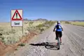 Radfahrer auf sandiger Strecke mit Warnschild.