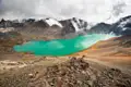 Türkisfarbener See in den Bergen mit schneebedeckten Gipfeln im Hintergrund.