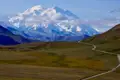 Panoramablick auf den Denali, den höchsten Berg Nordamerikas, mit einer Straße, die durch die Tundra-Landschaft im Vordergrund führt.