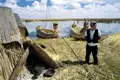 Traditionelle Schilfboote und -hütten der Uros auf dem Titicacasee. Ein Bewohner steht auf einer der schwimmenden Inseln.