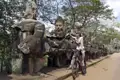 Reisende mit Fahrrad an den Steinfiguren von Angkor Thom.