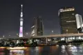 Der Tokyo Skytree bei Nacht, beleuchtet in rosa und weiß, mit umliegenden Gebäuden und einer Brücke über den Fluss.