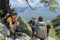 Wanderer machen eine Pause auf einem Bergpfad und genießen die Aussicht auf das Tal und die Bergkette.