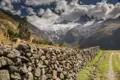 Blick auf die Anden mit Steinmauer und Hütte im Vordergrund.