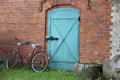 Rotes Fahrrad vor türkisfarbener Tür und roter Backsteinmauer.
