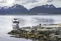 Ausflugsboot mit Touristen nähert sich einer felsigen Insel, auf der sich eine Gruppe von Seelöwen ausruht. Im Hintergrund ist die Berglandschaft von Ushuaia zu sehen.