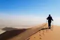 Person besteigt eine Sanddüne mit Wanderstöcken.