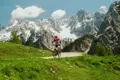 Mountainbiker auf einem Bergpfad mit schneebedeckten Alpengipfeln im Hintergrund.