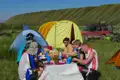 Reiseteilnehmer beim Mittagessen an einem Tisch vor Zelten. Ein Geländewagen steht im Hintergrund.