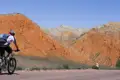Mountainbiker auf einer Straße mit roten und beigefarbenen Bergen im Hintergrund.