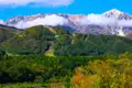 Herbstliche Berglandschaft mit Fluss und schneebedeckten Gipfeln im Hintergrund.