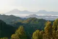 Panoramablick auf eine grüne Hügellandschaft mit Bergen im Hintergrund, die von Nebel durchzogen sind.