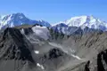 Ein Gletscher inmitten einer bergigen Landschaft mit schneebedeckten Gipfeln im Hintergrund.