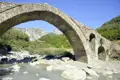 Alte Steinbrücke über einen Fluss in bergiger Landschaft.