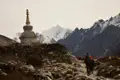Wanderer auf einem Bergpfad mit einem Stupa und schneebedeckten Bergen im Hintergrund.