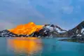Schneebedeckte Berge und Gletscher im goldenen Abendlicht, die sich im türkisfarbenen Wasser spiegeln.