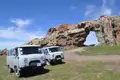 Reisebusse am Fuße eines Felsentors, welches Teil einer natürlichen Felsformation ist.