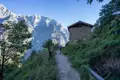 Wanderung auf einem Bergpfad mit Blick auf ein Steinhaus und schneebedeckte Berge.