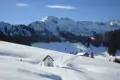 Verschneite Berglandschaft mit Kapelle und Hütte.