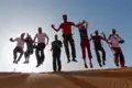 Reisegruppe springt freudig über eine Düne in der Wüste.
