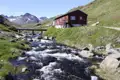 Ein Fluss fließt durch eine bergige Landschaft mit einer roten Hütte und einer Brücke im Vordergrund.