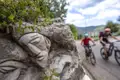 Nahaufnahme einer Steinskulptur, während Mountainbiker auf einem Weg im Hintergrund fahren.
