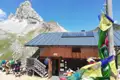 Berghütte in den Bergen mit Solarpanelen und Gebetsfahnen, im Hintergrund ein Berg.