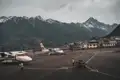 Flugzeuge auf einem Bergflughafen mit schneebedeckten Gipfeln im Hintergrund.