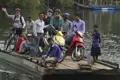 Reisende und Einheimische überqueren einen Fluss auf einer Fähre. Fahrräder und Motorroller werden transportiert.