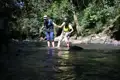 Zwei Wanderer überqueren einen Fluss, indem sie sich gegenseitig Halt geben und auf Steine im Wasser treten.