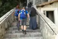 Wanderer und Nonnen besteigen eine Steintreppe, möglicherweise im Rahmen einer Pilgerreise oder eines Besuchs eines religiösen Ortes.