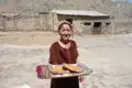 Frau mit traditionellem Fladenbrot vor einem Haus.