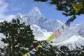 Bunte Gebetsfahnen im Vordergrund mit Blick auf einen schneebedeckten Berg im Himalaya.