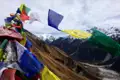 Gebetsfahnen im Vordergrund, dahinter schneebedeckte Berge und ein Tal.