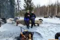 Zwei Reisende wärmen sich an einem Lagerfeuer während einer Pause von ihrer Schneemobiltour im verschneiten Wald.