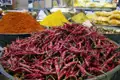 Getrocknete rote Chilischoten in einer Schüssel auf einem Markt, umgeben von anderen Gewürzen.