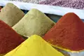 Verschiedene Gewürze, darunter rot, gelb und grün, pyramidenförmig auf einem Marktstand angeordnet.