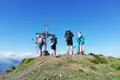 Wanderer mit Rucksäcken stehen am Gipfelkreuz und blicken in die Ferne.