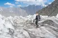 Wanderer mit Rucksack und Wanderstöcken überquert einen Gletscher vor der Kulisse schneebedeckter Berge.
