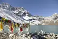Bunte Gebetsfahnen am Ufer eines Bergsees mit schneebedeckten Himalaya-Gipfeln im Hintergrund.