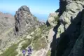 Wanderer auf einem Bergpfad mit felsigen Gipfeln im Hintergrund.