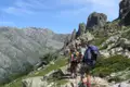 Wandergruppe auf einem Bergpfad mit felsigen Gipfeln im Hintergrund.