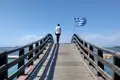 Holzbrücke mit griechischer Flagge und Blick aufs Meer.