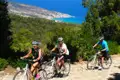 Drei Radfahrer genießen eine Radtour auf einem Küstenweg mit Blick auf das Meer und die Hügel.