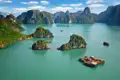 Panorama der Halong-Bucht mit bewaldeten Kalksteininseln und mehreren traditionellen Dschunken.